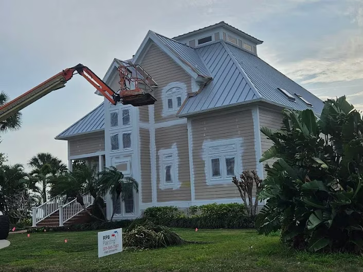 Large coastal home exterior painting in progress with boom lift at dusk by RPB Painting